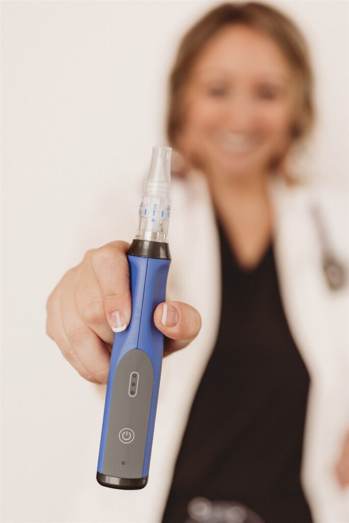Deborah Daniels NP is out of focus, her right hand is manicured in a french manicure and she is holding a blue SkinPen Precision. She is smiling because her mom's skin is gorgeous after having the SkinPen!