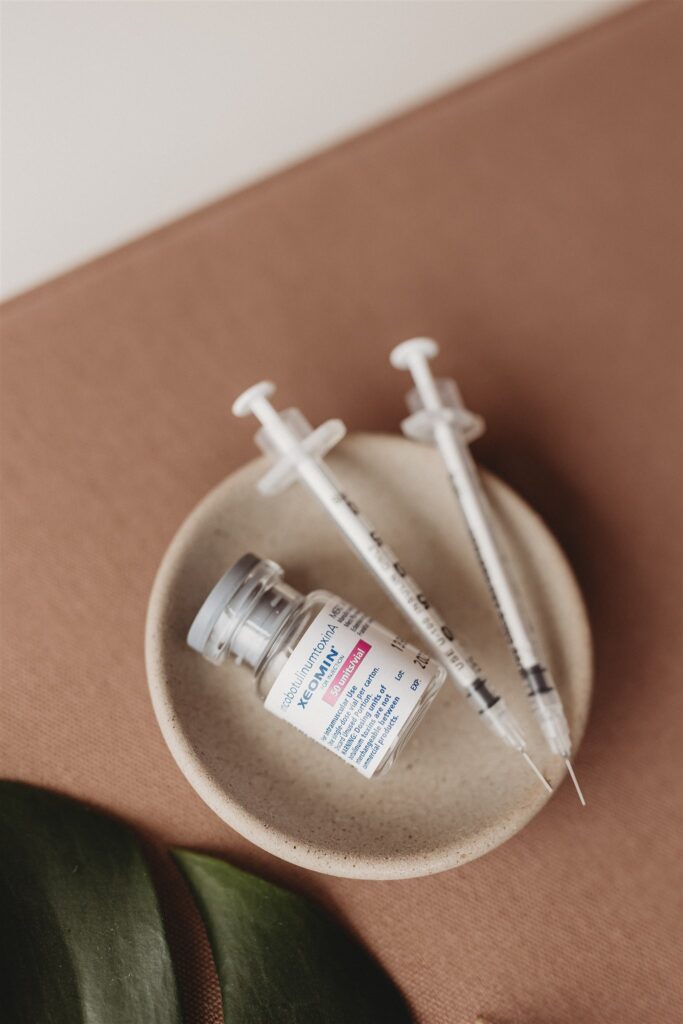 Brown background with small cream bowl containing two insulin syringes and a vial with a white label and in blue writing "incobotulinumtoxinA XEOMIN" is written. It is the "clean tox" and is used like Botox. Botox and Xeomin have similar dosing. 