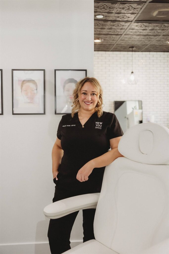 Deborah Daniels, NP at New You Health, smiling confidently while standing next to a treatment chair.