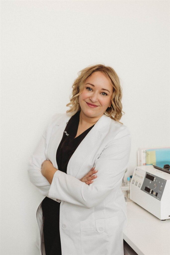 Deborah Daniels, NP, standing confidently in a white coat with arms crossed in front of a white background.