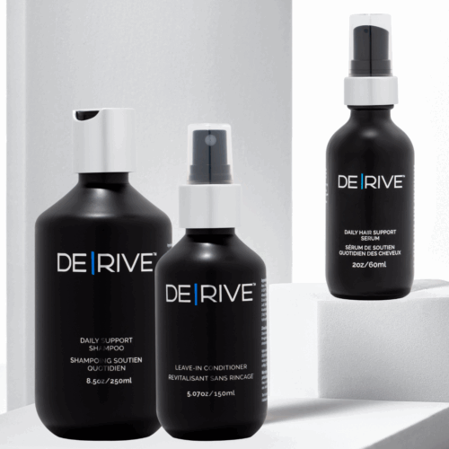 Three DERIVE hair restoration products — Daily Support Shampoo (8.5 oz), Leave-In Conditioner (5.07 oz), and Daily Hair Support Serum (2 oz) — shown on white minimalist blocks with soft lighting, highlighting their sleek black packaging and modern aesthetic.